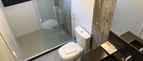 Un baño moderno con cabina de ducha de vidrio, un inodoro y un lavabo sobre un mueble negro.