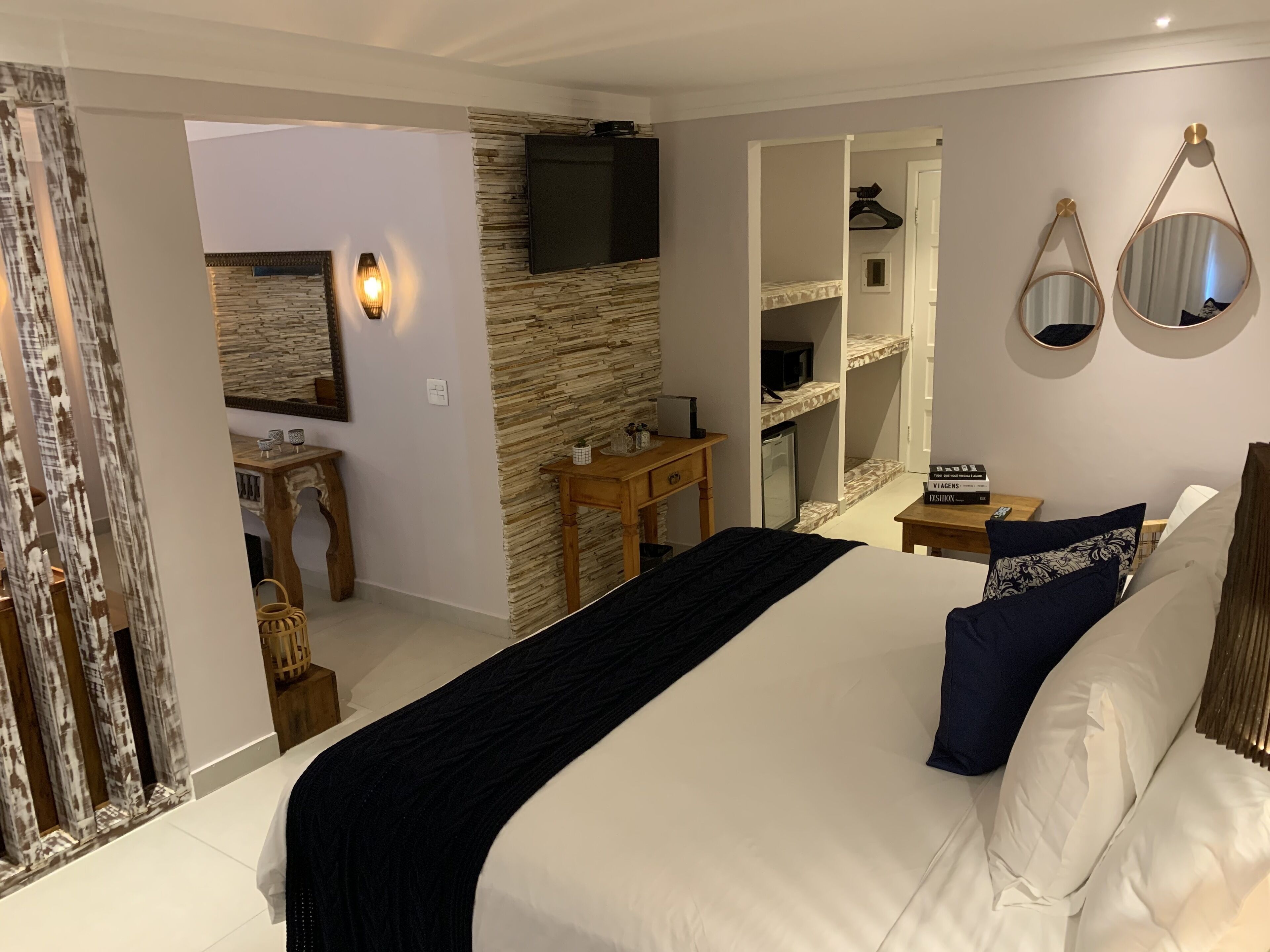 A modern bedroom with a large bed, a desk, a wardrobe, and a TV mounted on a stone wall.