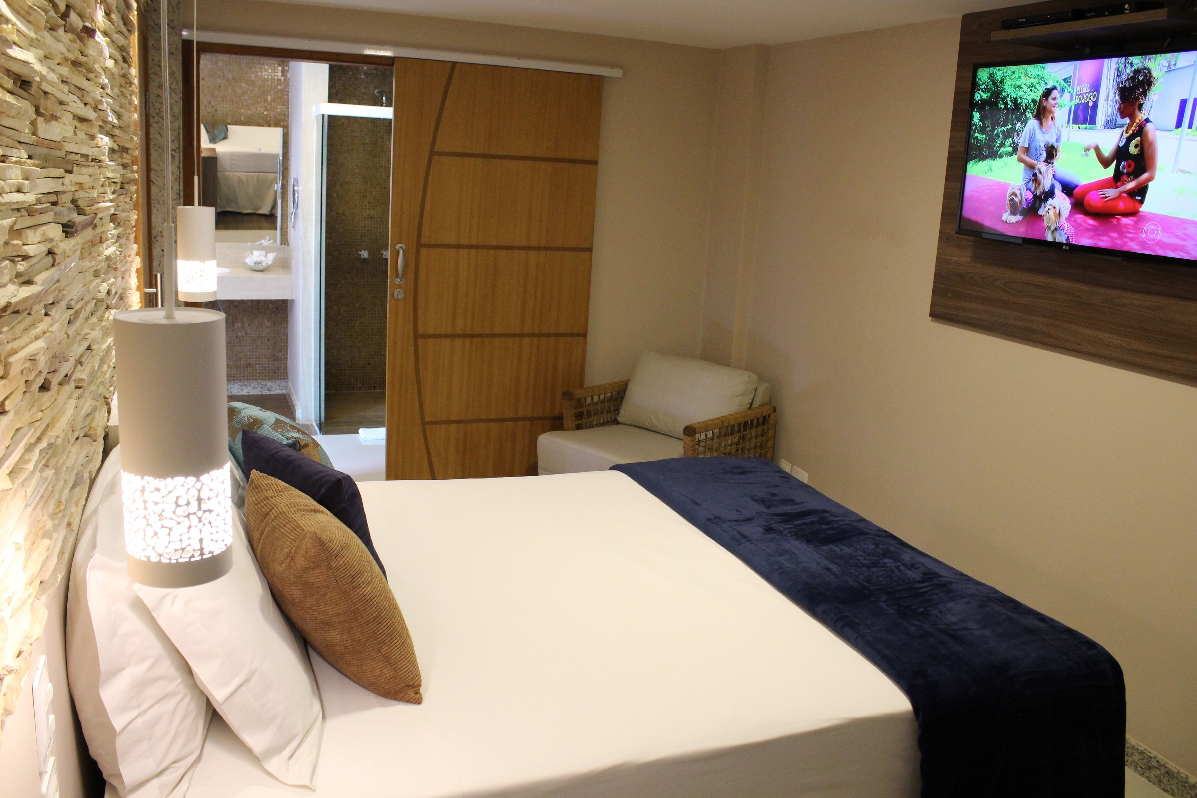 Una habitación de hotel con una cama, televisión, puerta de madera y pared con un diseño texturizado.