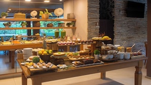 A buffet with a variety of food items and a wooden table. - Hotel Experience João Fernandes (Búzios)