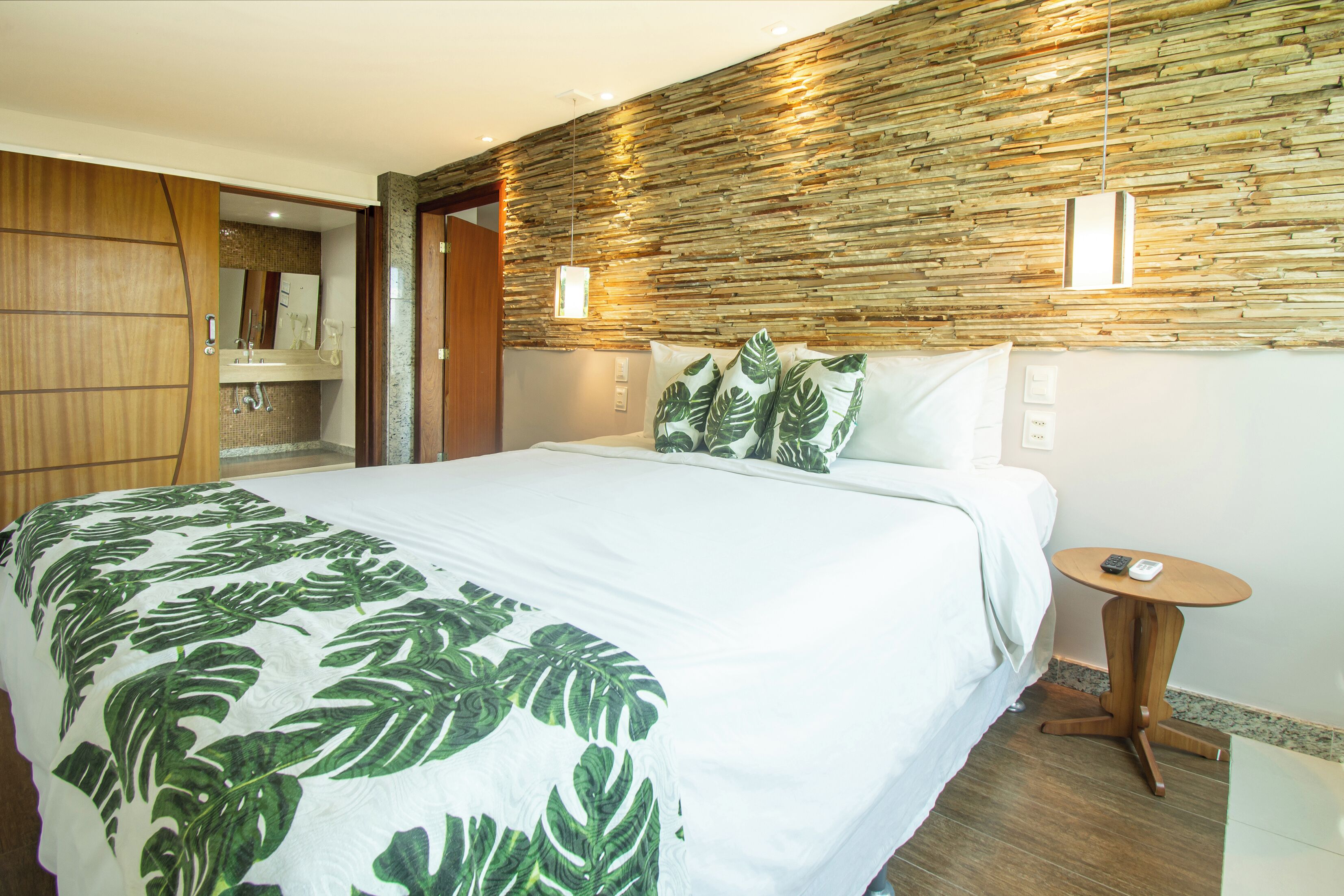 A hotel room with a bed, a wooden wardrobe, a bathroom with a mirror, and a wall with a textured pattern.