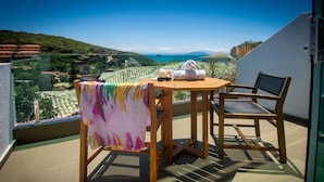 A balcony with a wooden table and chair, a towel, and a view of the sea and hills. - Hotel Experience João Fernandes (Búzios)