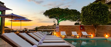 Una piscina al aire libre, sombrillas, sillones reclinables de piscina