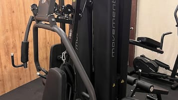 A gym with various exercise equipment, including a cable machine and weight benches.