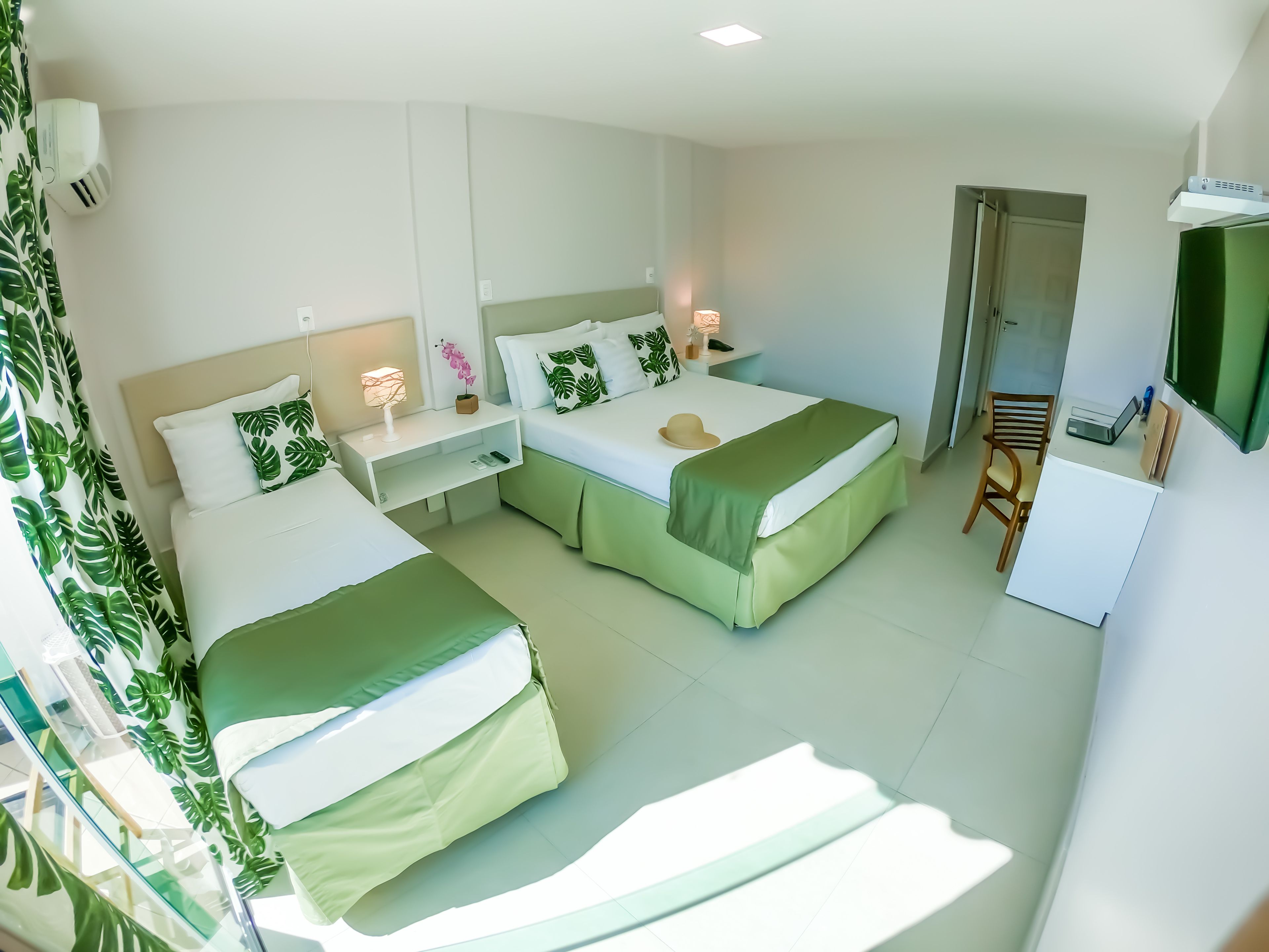 A hotel room with two beds, a desk, a chair, a TV, and a door.