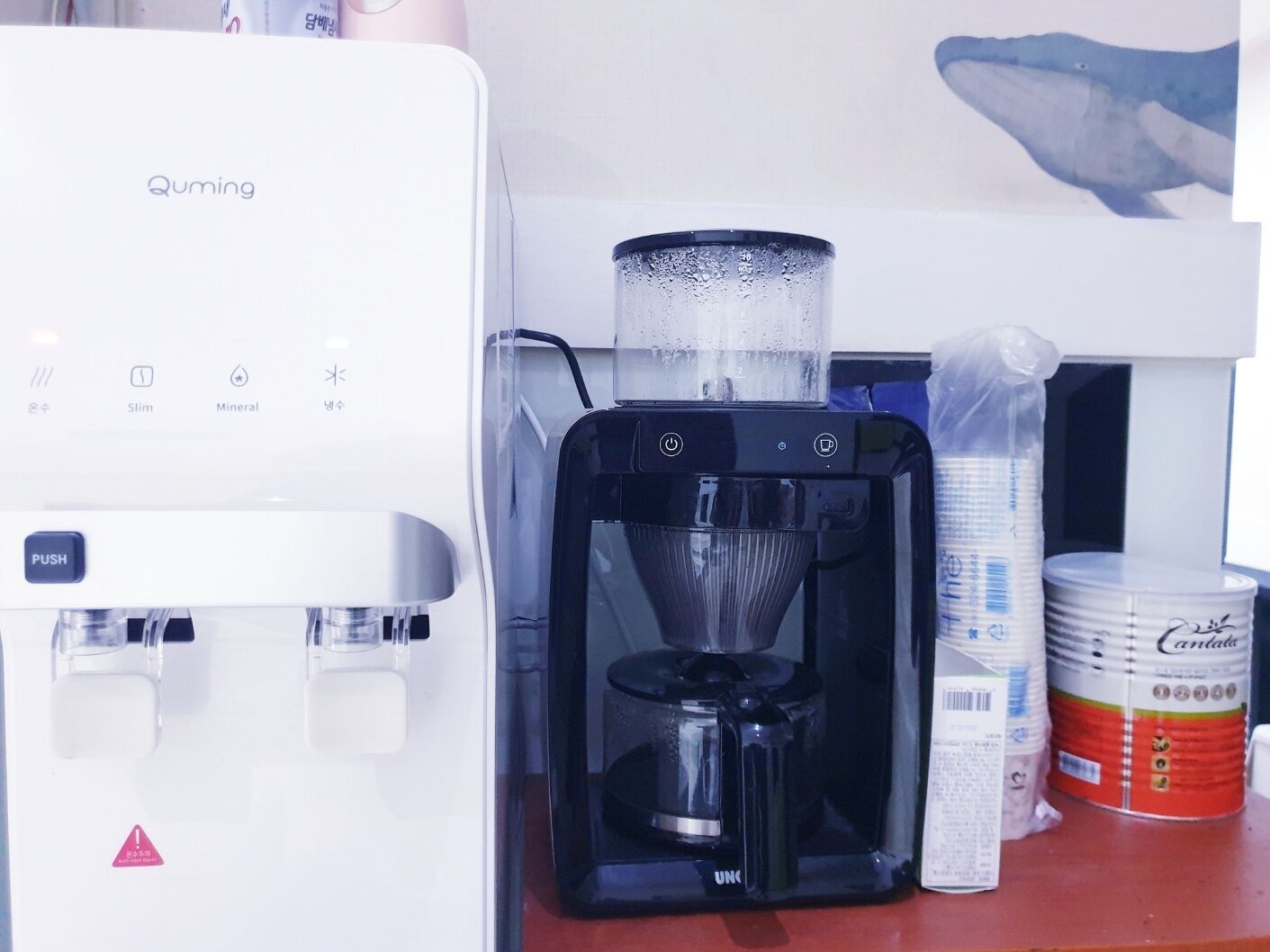 A coffee machine, a water dispenser, and a can of condensed milk on a counter.