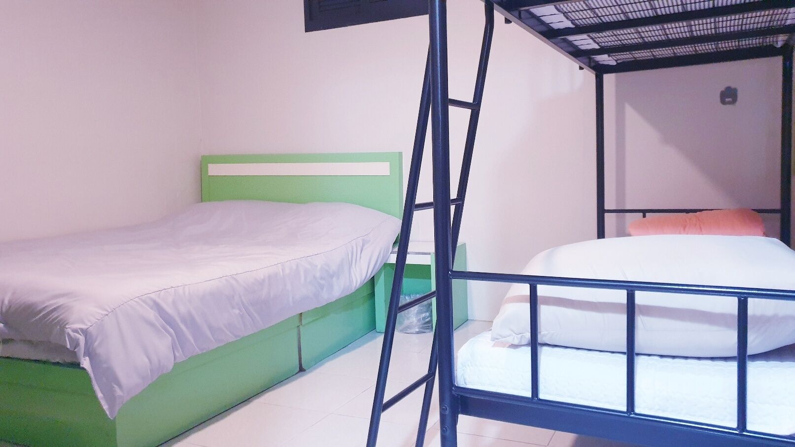 A dormitory room with two bunk beds, one with a green headboard and the other with a white headboard.