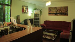 Una sala de estar con un mostrador de recepción de madera, un sofá rojo, una mesa de centro de cristal, una estantería, un cuadro en la pared y una ventana con vistas a árboles.