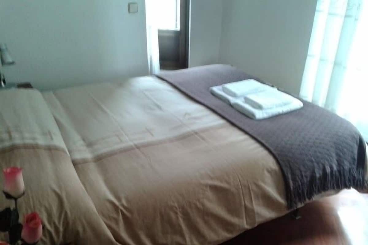 A neatly made bed with a beige comforter and a brown blanket, a white pillow, and a folded white towel.