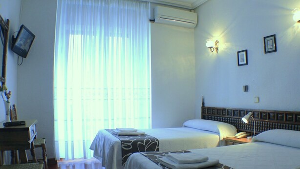 Habitación de hotel con dos camas, un escritorio, una silla, un equipo de aire acondicionado y una ventana con cortinas.