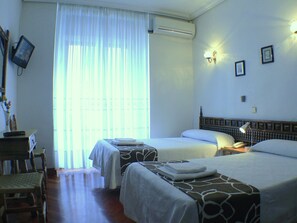 Quarto de hotel com duas camas, uma escrivaninha, uma cadeira, aparelho de ar condicionado e janela com cortinas.