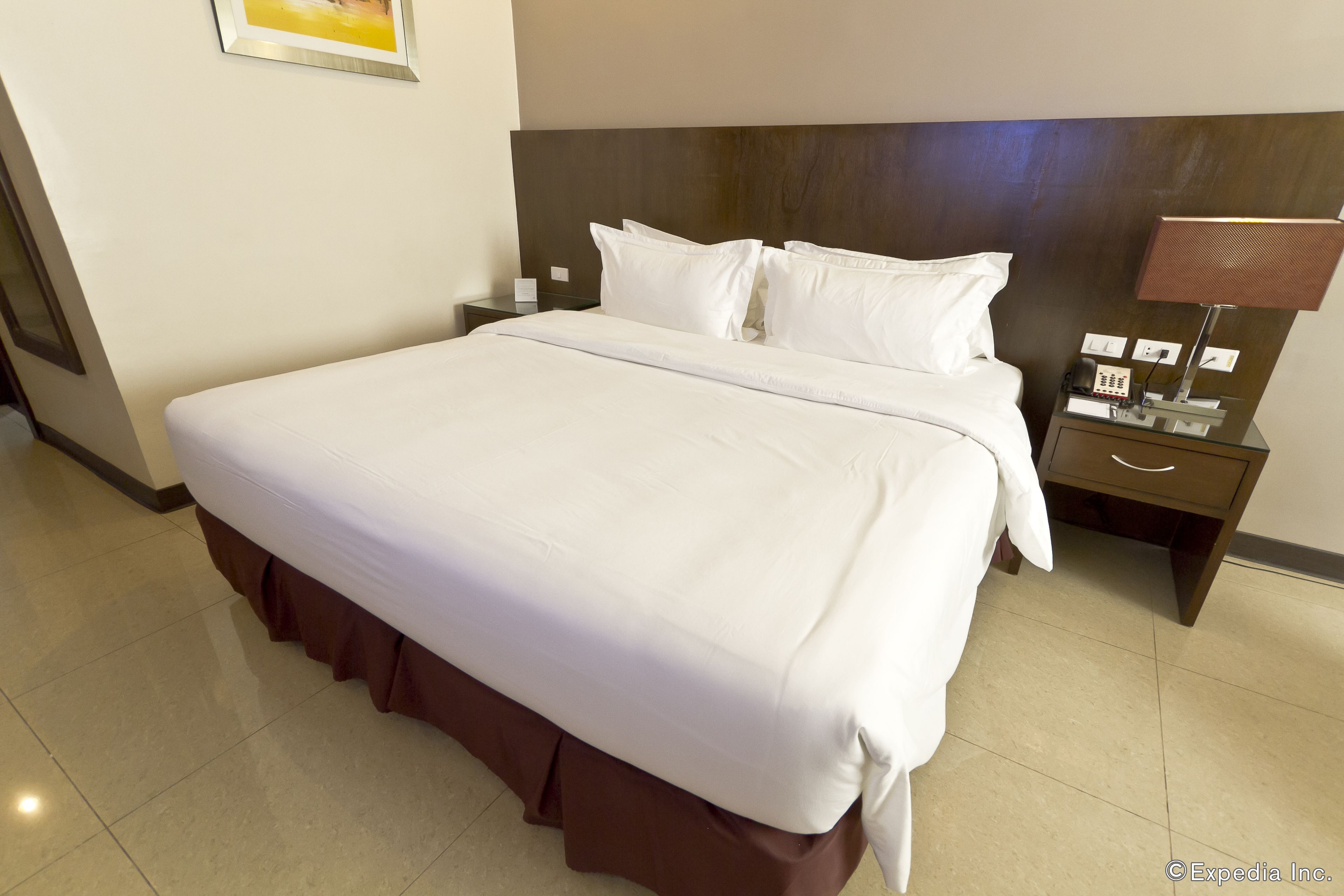 A hotel room with a large bed, a nightstand, a lamp, and a framed picture on the wall.