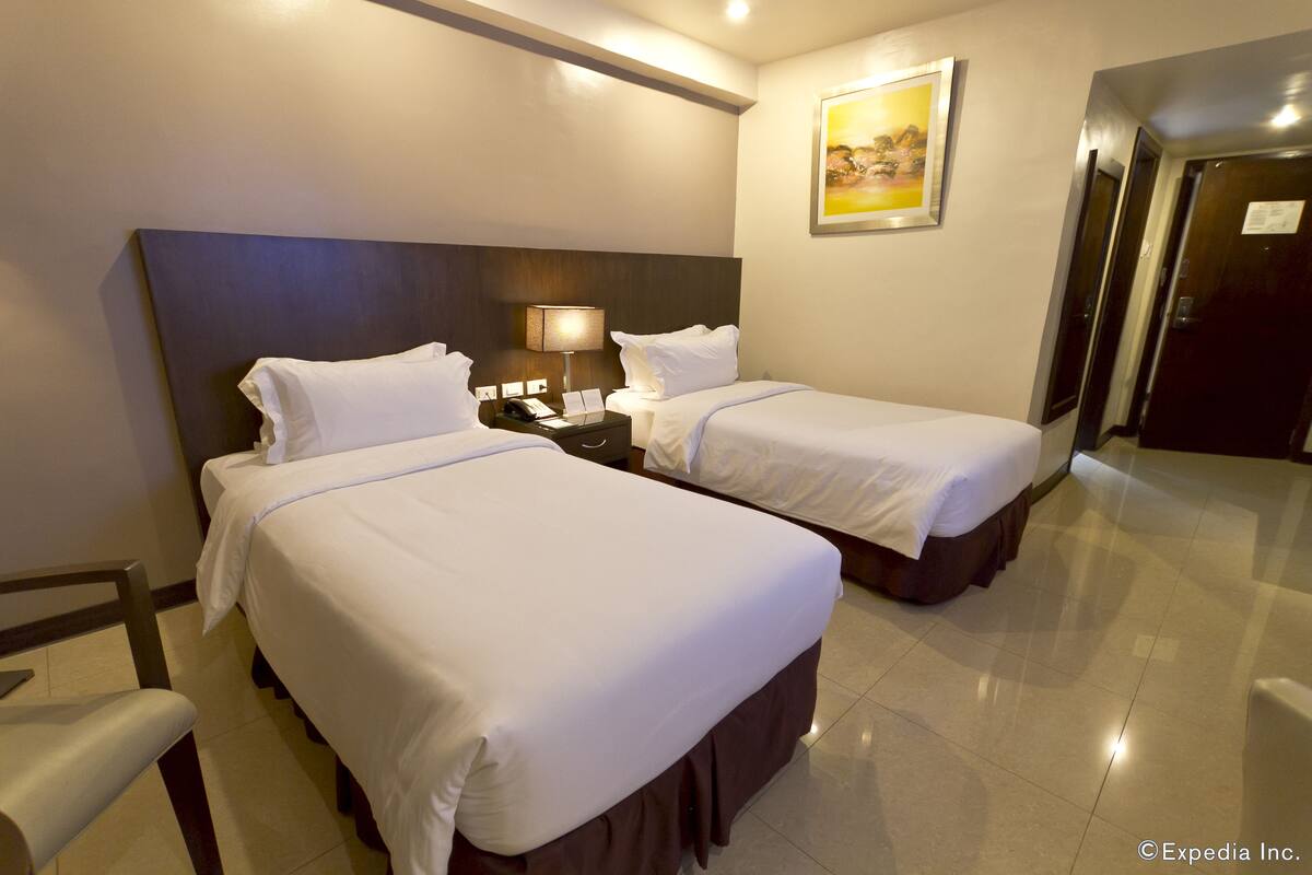 Una habitación de hotel con dos camas, una mesita de noche, una lámpara y un cuadro en la pared.