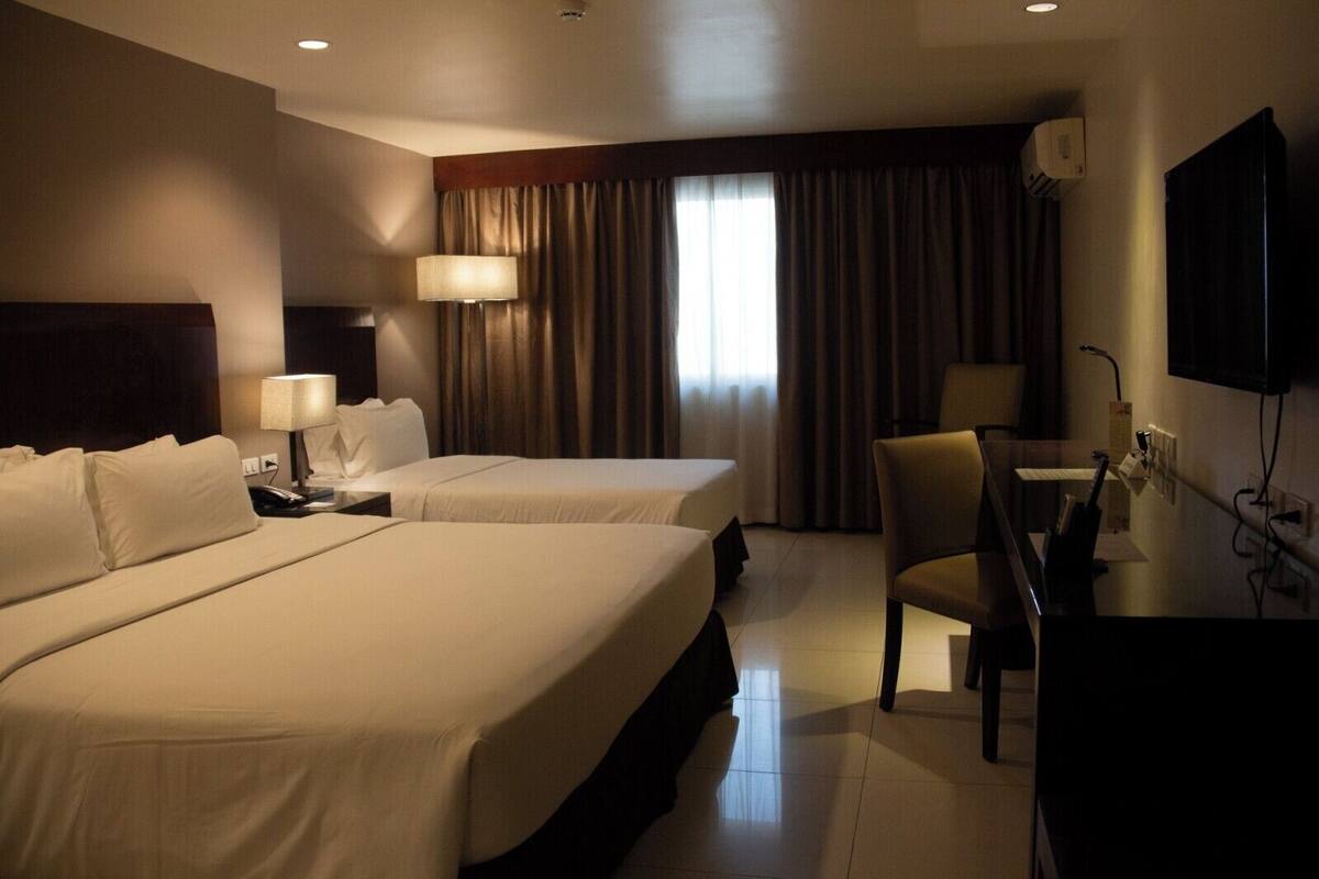 Habitación de hotel con dos camas, un escritorio con silla, televisor y ventana con cortinas.