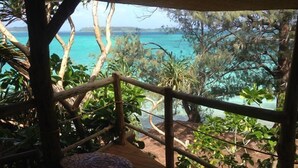 Eine Holzterrasse mit Geländer, die auf ein türkisblaues Meer und üppiges Grün blickt.