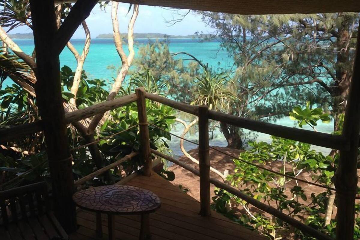 A wooden deck with a railing overlooking a turquoise sea and lush greenery.