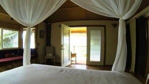 Ein Schlafzimmer mit einem großen Bett, einem Sessel, einem Schreibtisch und einer Glastür zu einem Außenbereich.
