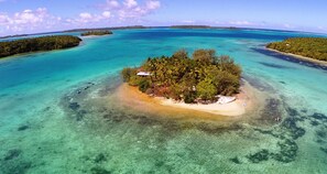 Vista aérea de una isla tropical con aguas turquesas cristalinas, rodeada de exuberante vegetación y algunos edificios pequeños.