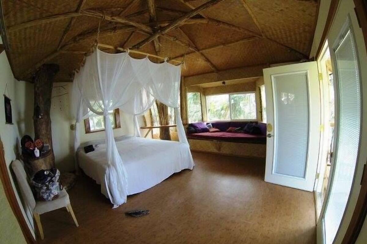A room with a bed under a canopy, a bench with cushions, and a door leading outside.