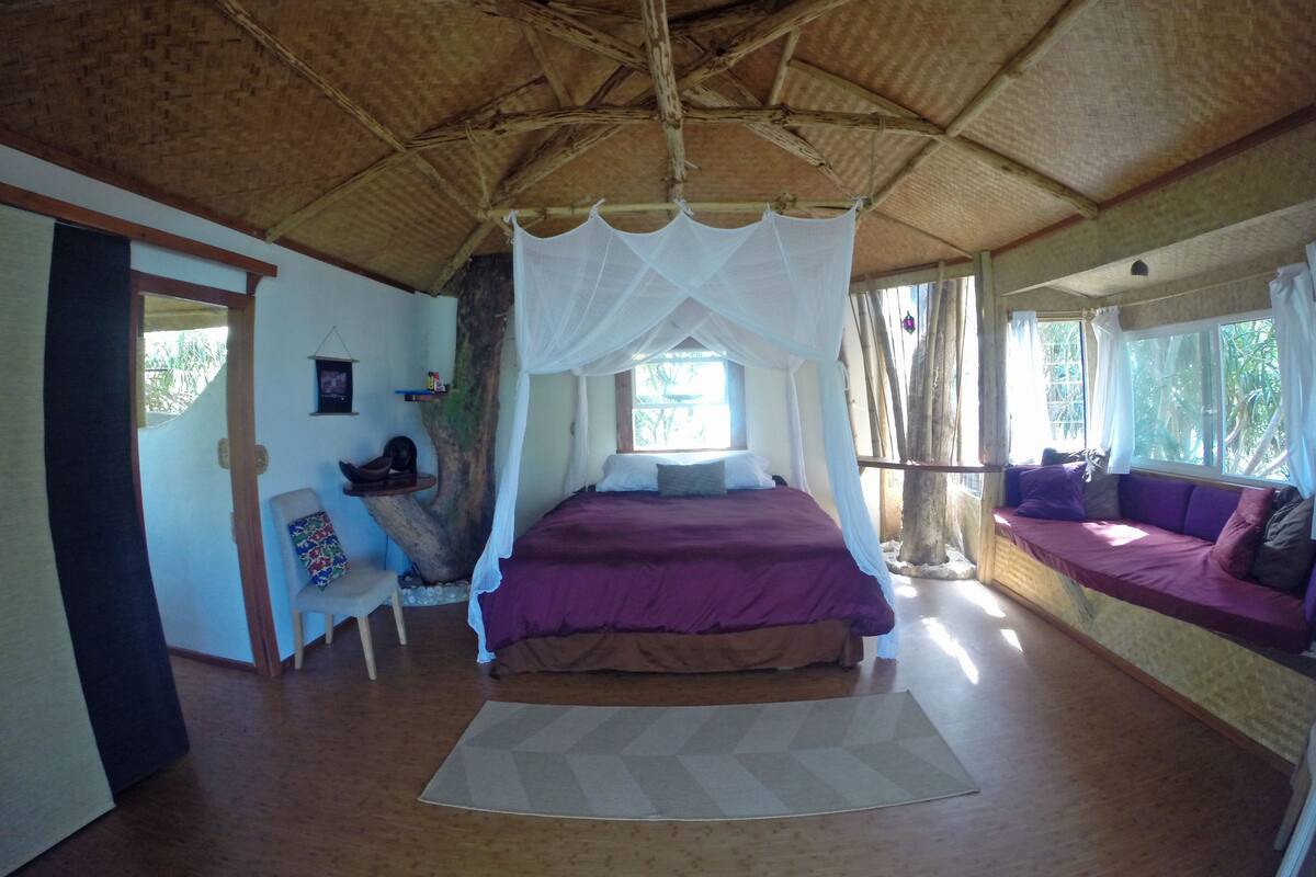 A room with a bed under a canopy, a sofa, a chair, and a small table.