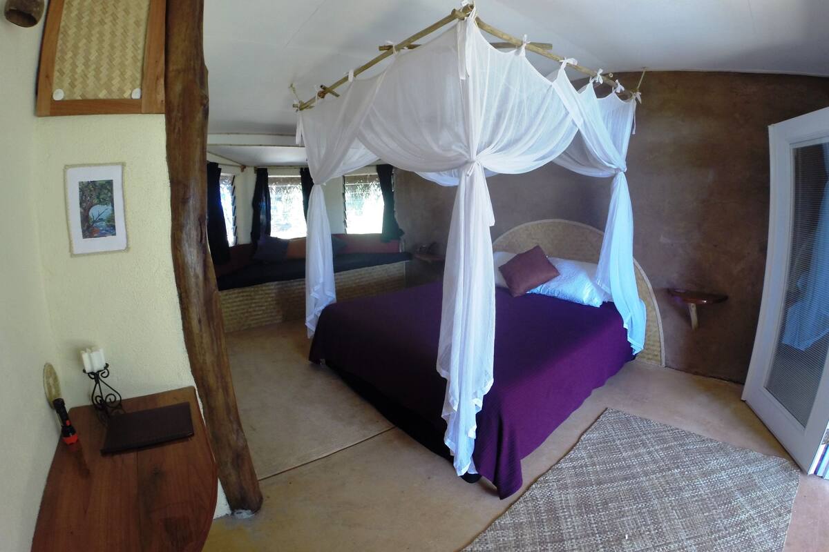 A room with a bed under a canopy, a picture on the wall, and a wooden bench.