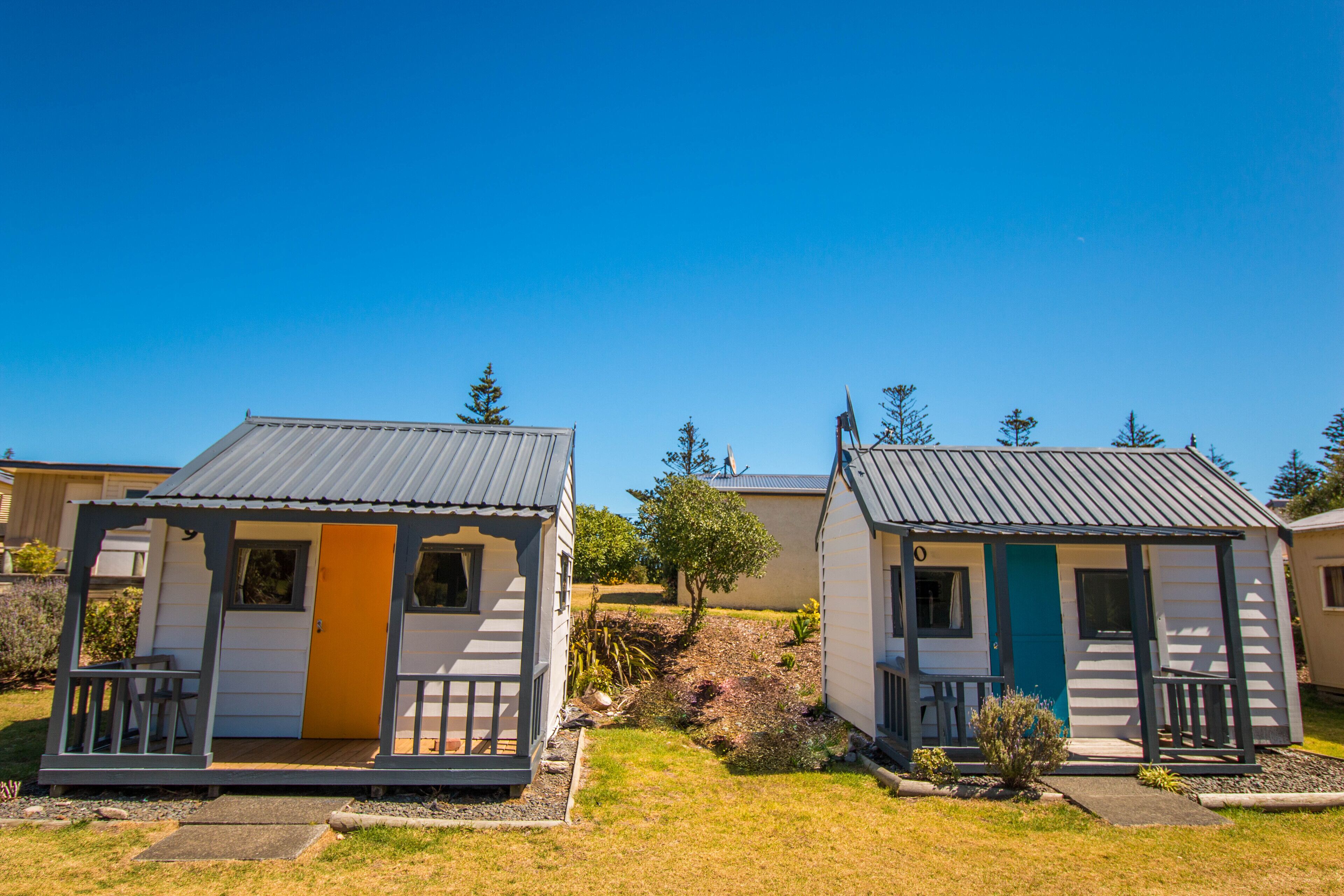 Two small, single-story cabins with a metal roof, a front porch, and a door.