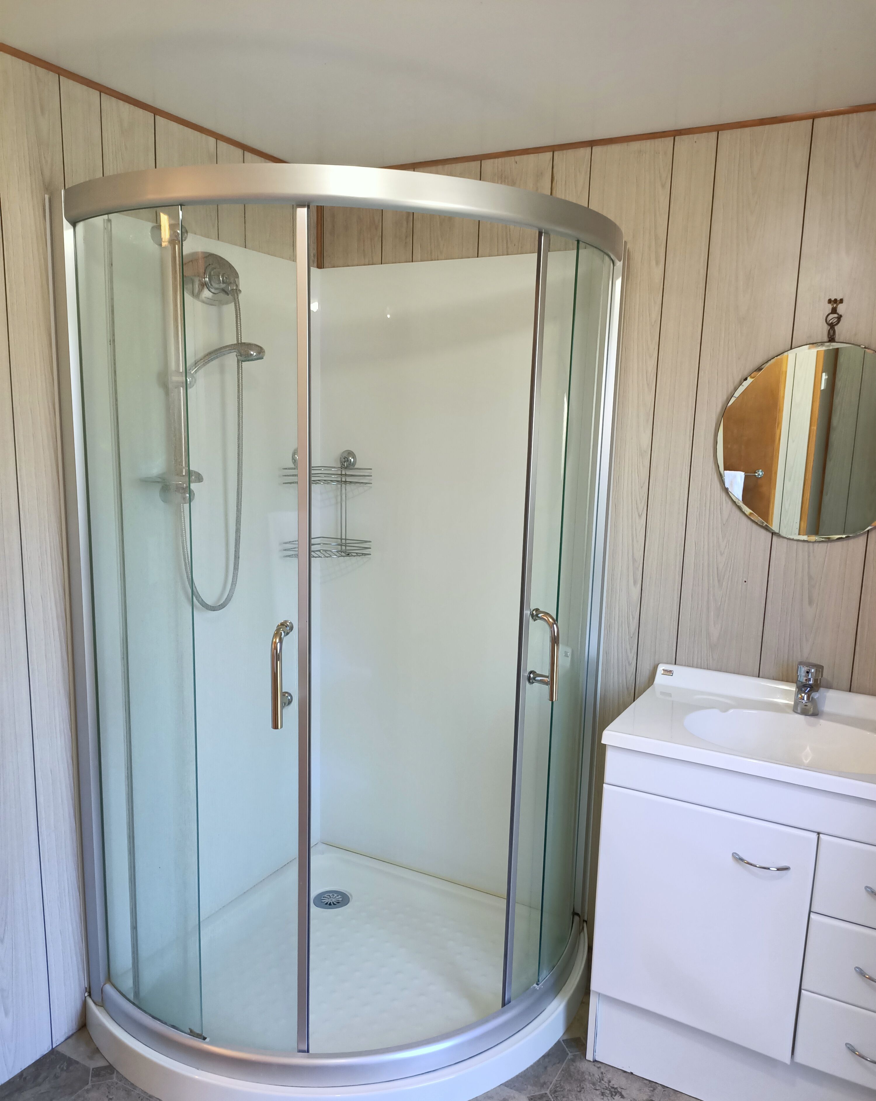 Une cabine de douche fermée par des parois en verre, avec un meuble-lavabo blanc et un miroir.