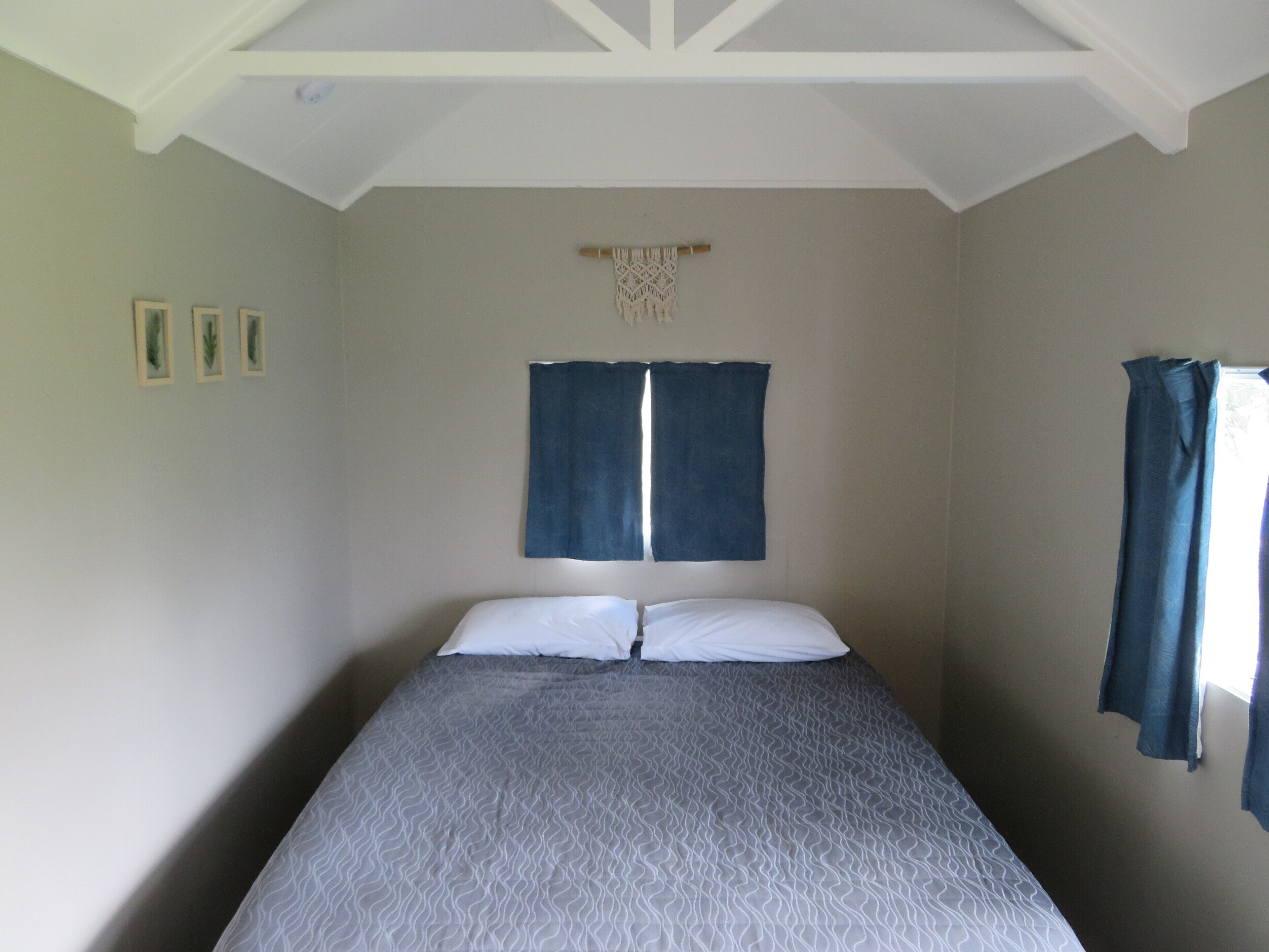 Una cama individual con una colcha estampada, dos almohadas y una ventana con cortinas azules.