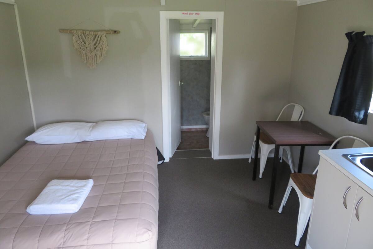 Een kamer met een bed, een bureau, een stoel, een wastafel en een deur naar een badkamer.