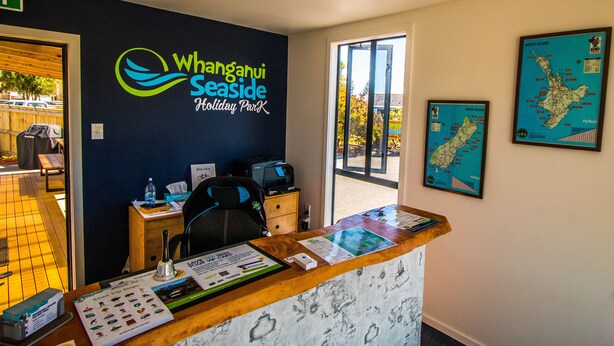 Ein Empfangsschalter im Whangāhui Seaside Holiday Park, an der Wand hängt eine Karte von Nord- und Südinsel.