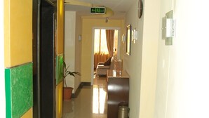 A hotel corridor with a reception desk, a clock, and a sign indicating the exit.