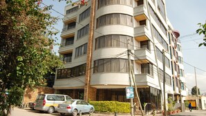 A multi-story building with balconies, a parking area, and a signboard.