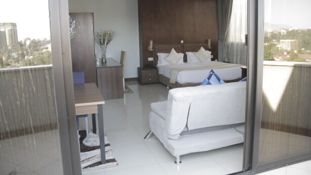 A modern hotel room with a large bed, a sofa, a desk, and a view of the city.