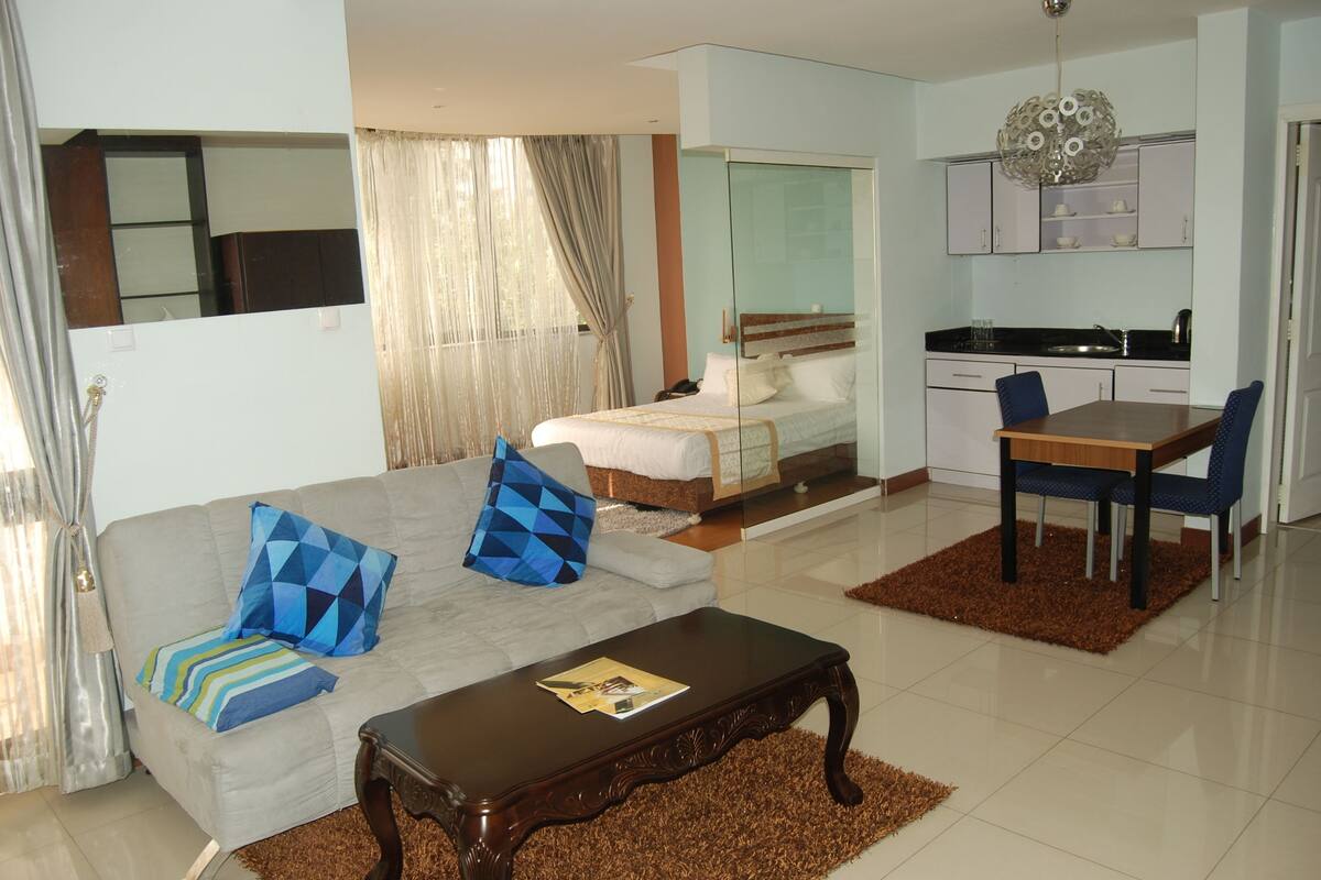A modern hotel room with a sofa, a bed, a dining table, and a kitchen area.