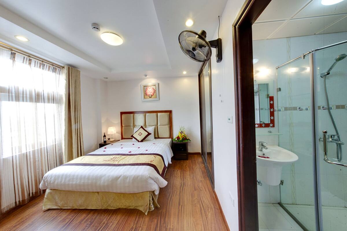 Habitación de hotel con cama, mesita de noche, lámpara y zona de ducha.