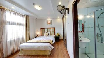 A hotel room with a bed, bedside table, lamp, and a shower area.