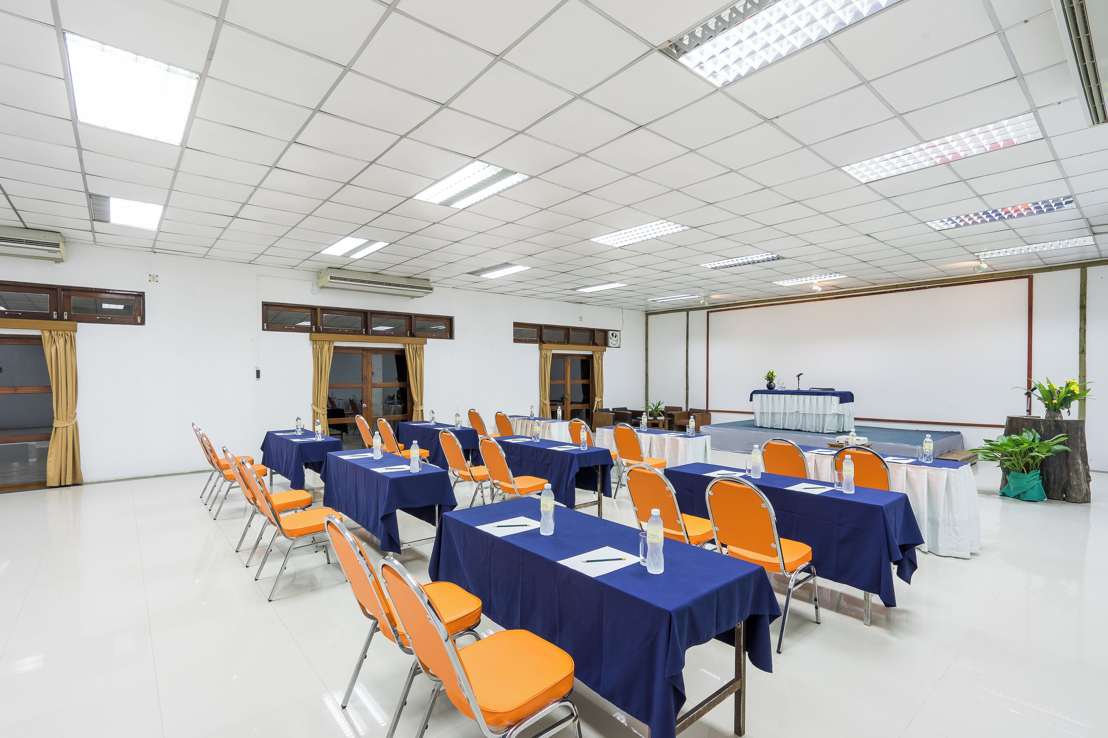 Una sala conferenze con tavoli e sedie, condizionatori e uno schermo di proiezione.