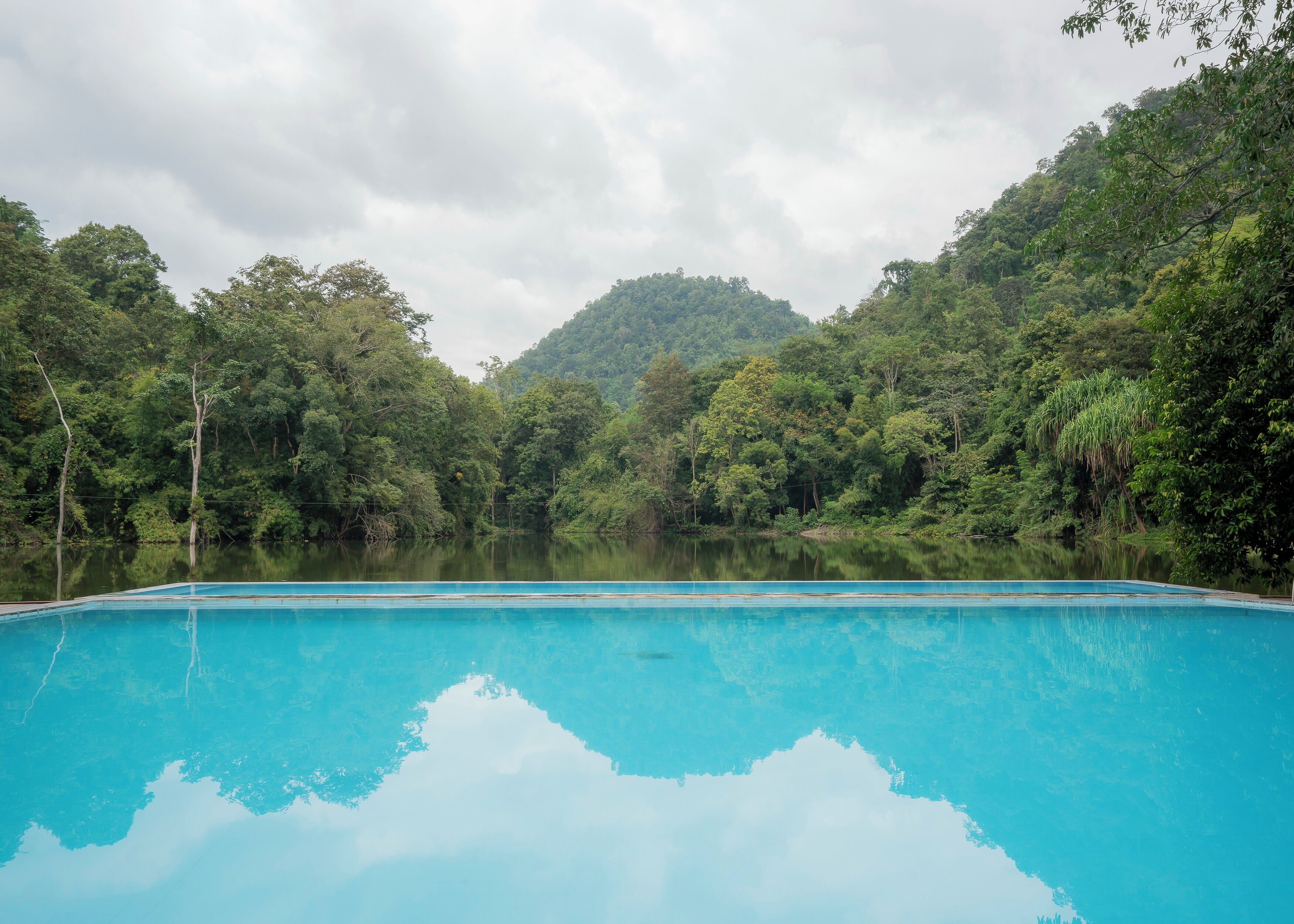 A clear blue pool surrounded by lush green forest and hills.
