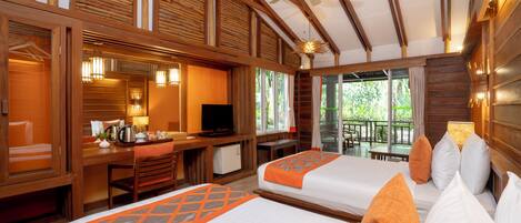 A hotel room with two beds, a desk, a television, and a balcony with a view of greenery.