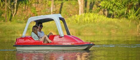 Un barco rojo y blanco con dos personas navegando sobre aguas tranquilas, rodeado de vegetación.