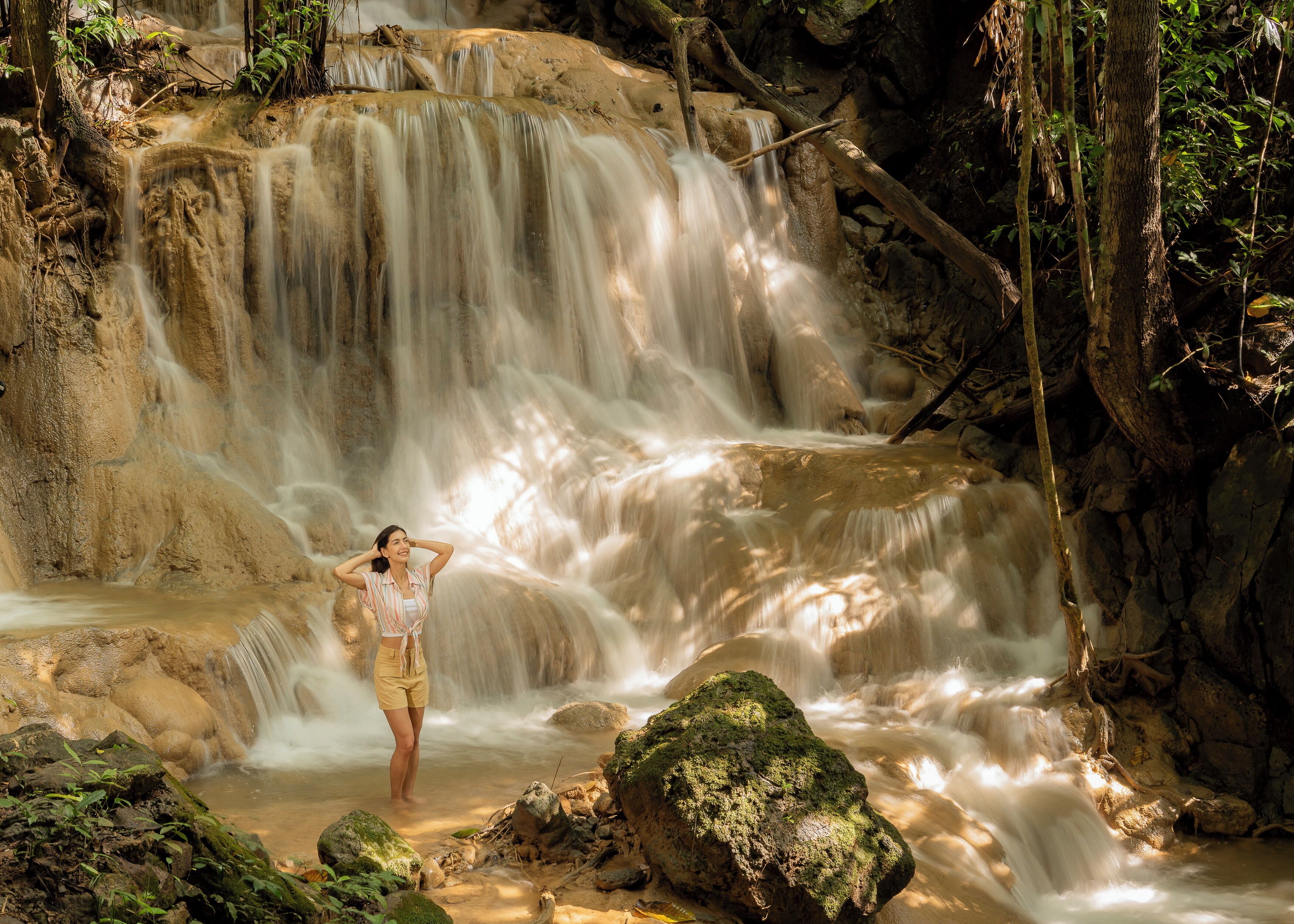 A waterfall in a natural setting with a person standing in the foreground.