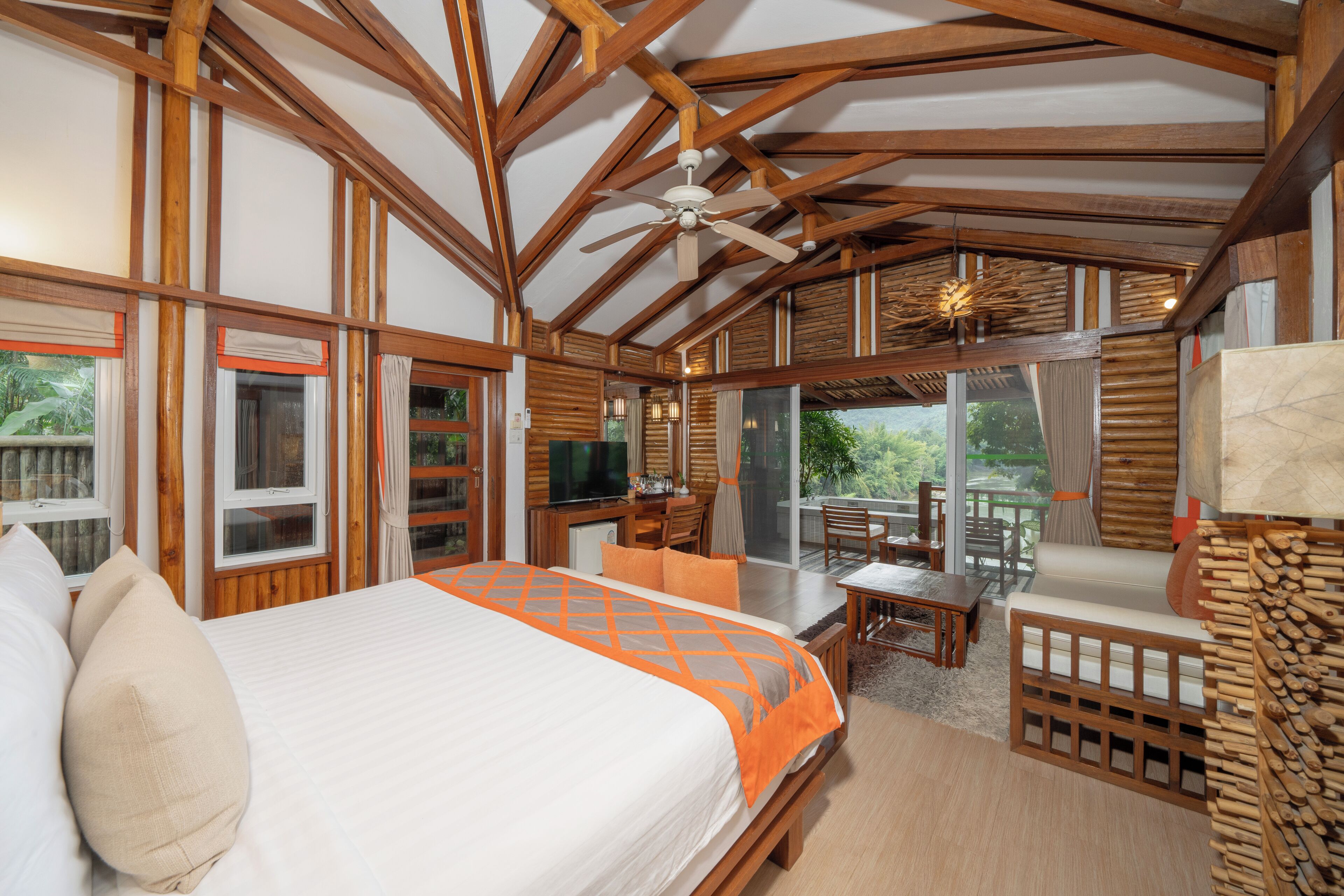 A spacious bedroom with a large bed, wooden ceiling beams, a ceiling fan, and a view of the outdoors.
