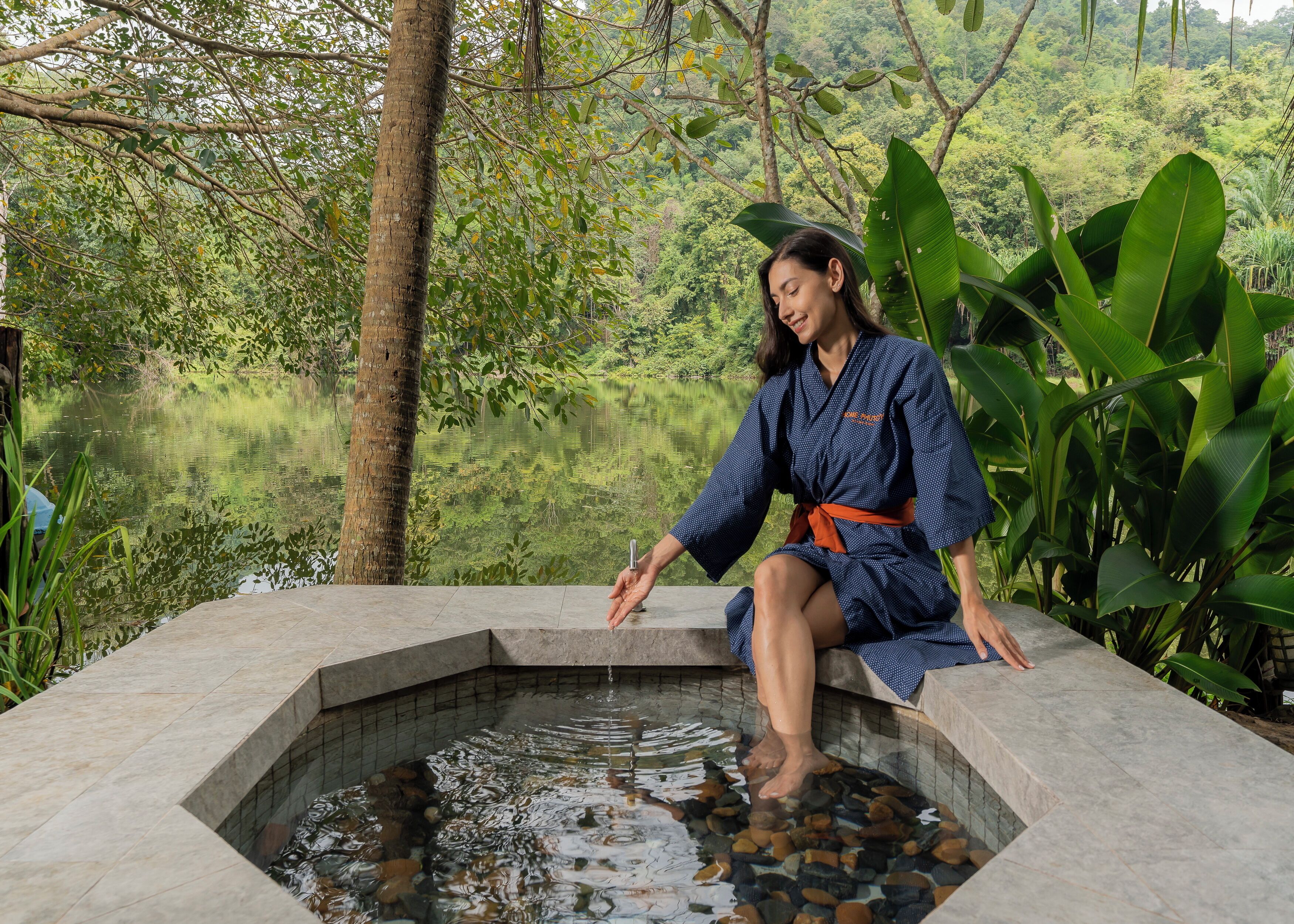 A person sitting by a stone pool surrounded by lush greenery.
