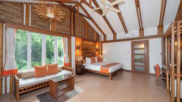Una habitación amplia con una cama grande, una zona de estar con vistas al exterior y un ventilador de techo.