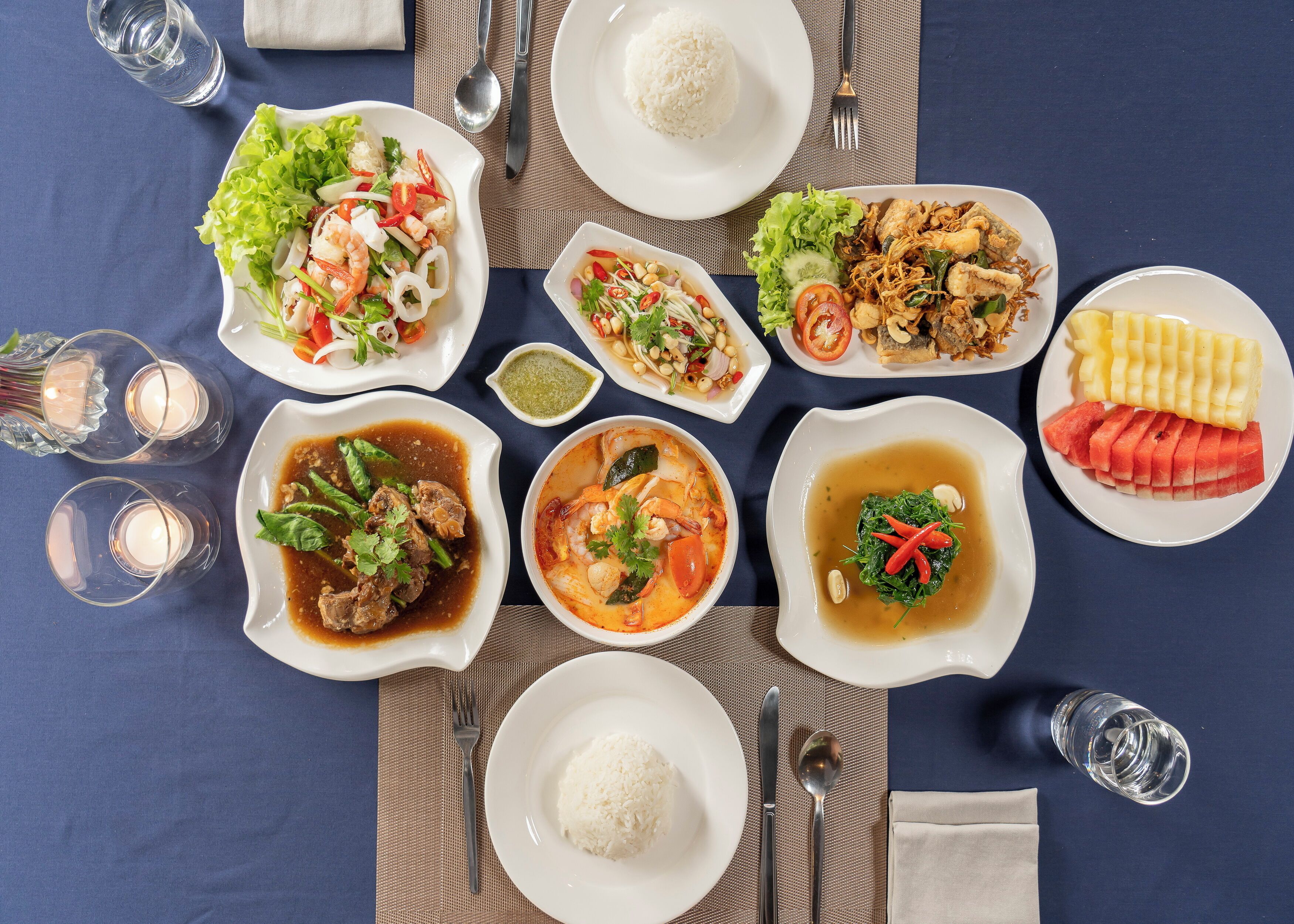 Una mesa dispuesta con diversos platos, incluyendo arroz, ensaladas y sopa, junto con vasos y cubiertos.