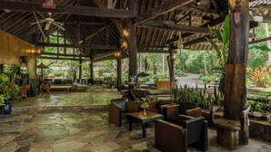 A spacious outdoor area with stone flooring, wooden furniture, and a thatched roof structure.