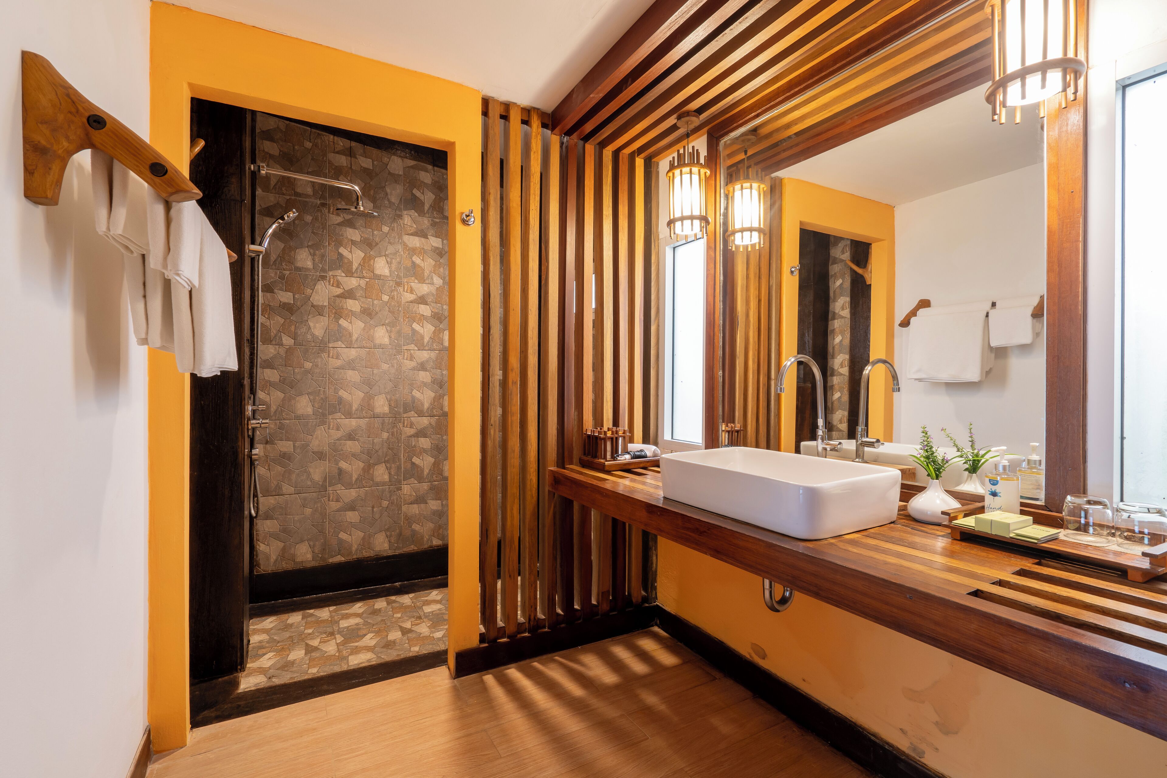 A modern bathroom with a wooden vanity, a large mirror, and a shower with a stone wall.