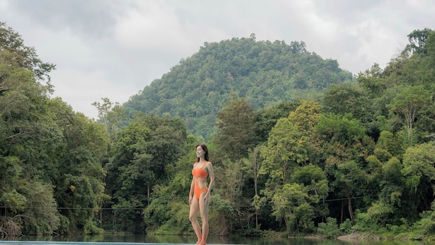 A woman standing by a pool with a forested hill in the background.