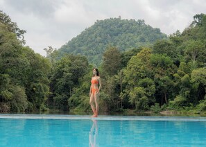 A woman standing by a pool with a forested hill in the background. - Home Phutoey River Kwai Hotspring & Nature Resort (Sai Yok)
