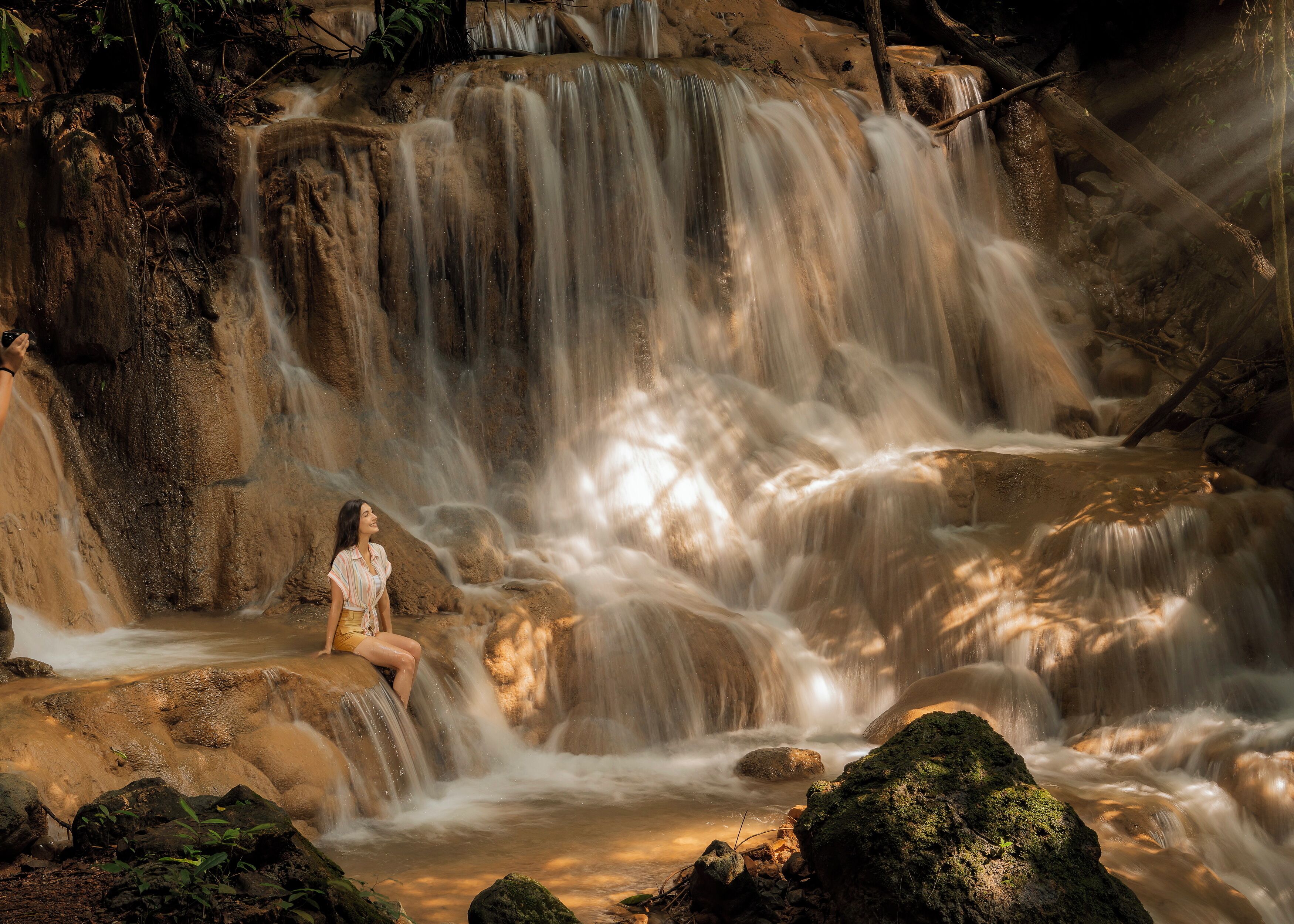 A waterfall with a person sitting on a rock.